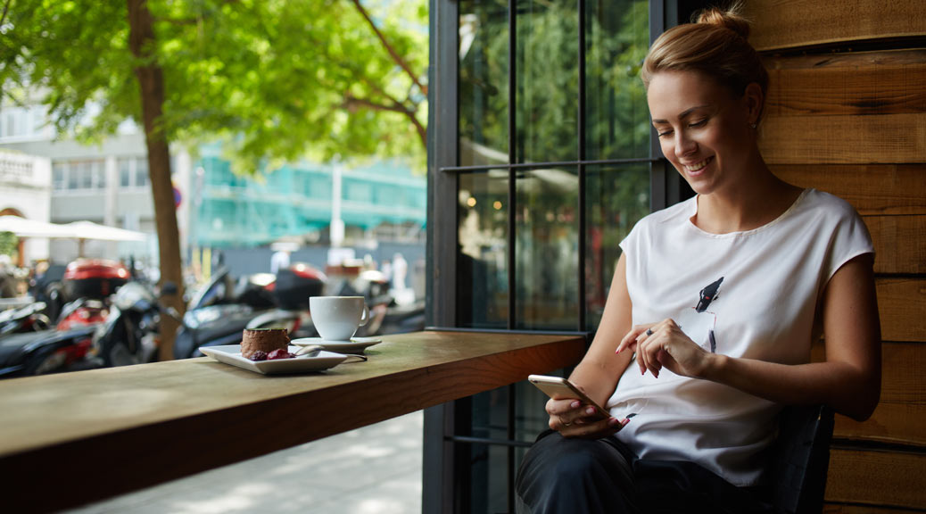 Charming woman with beautiful smile reading on mobile phone in coffee shop.