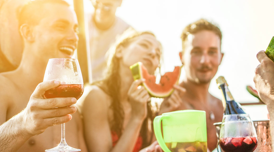 Happy friends drinking sangria wine and eating watermelon at boat party 