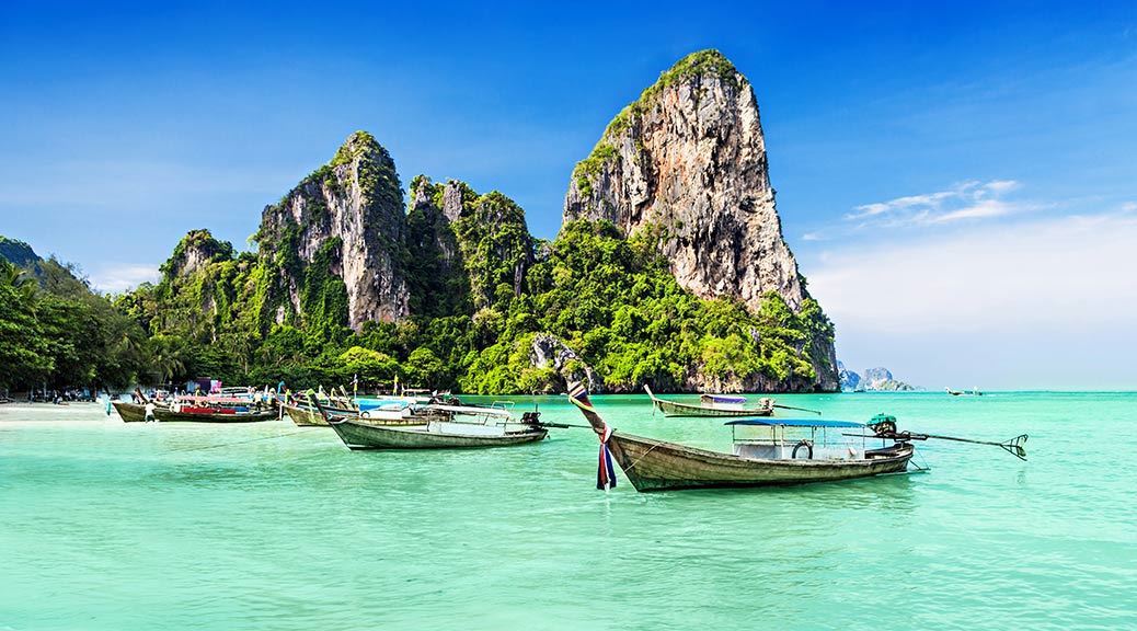 Longtail Boats in the clear sea green water with tall mountains close to the beach