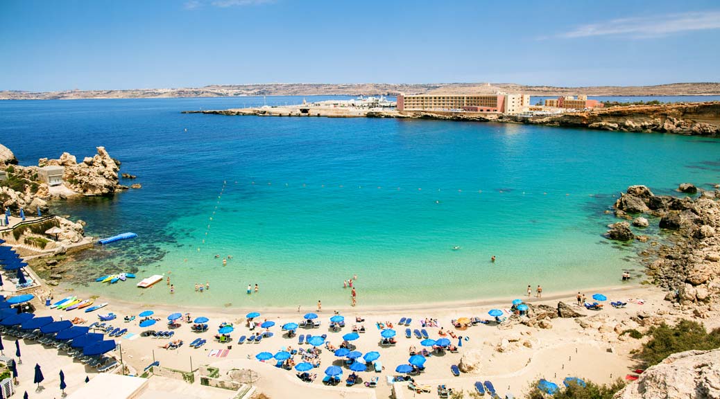 blue umbrella on tropical beach with white sand turquoise sea water and blue sky at deserted island in Malta Paradise bay