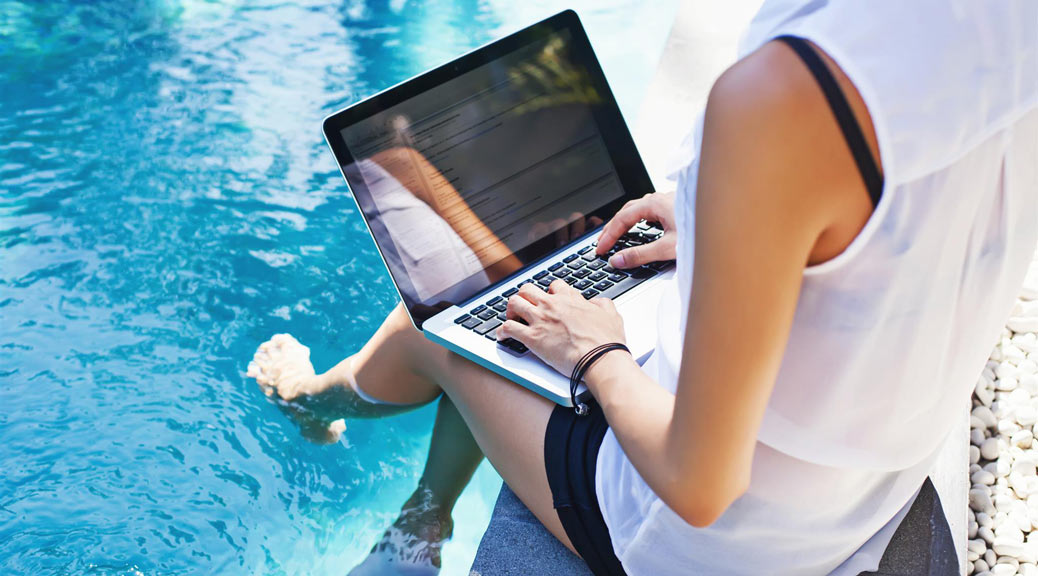 Woman working on her laptop computer sitting at poolside