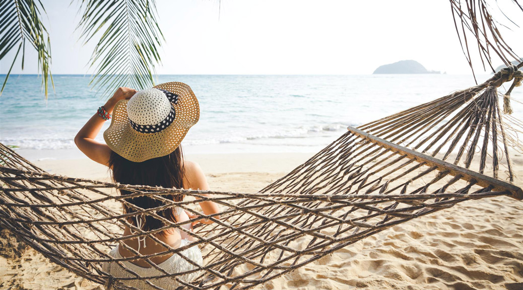 appy woman with white bikini, hat and shorts Jeans relaxing in hammock on tropical beach at sunset