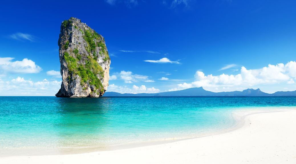 Huge rock standing tall in the middle of the ocean partially covered with green in a clear weather