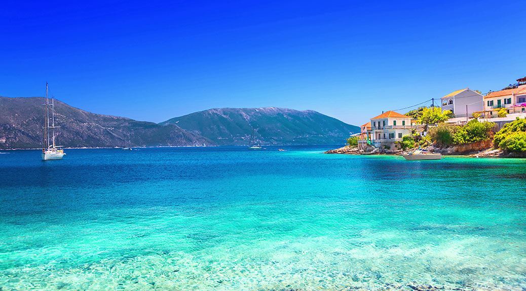 Mountains and sail boats in the clear calm blue water surrounding small fiskardo village