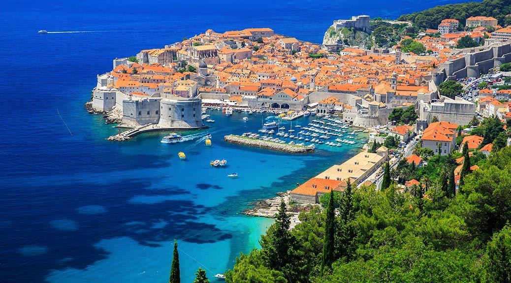 Picturesque view through the trees of the old town and boats docked at the pier of Dalmatian Coast of Adriatic Sea